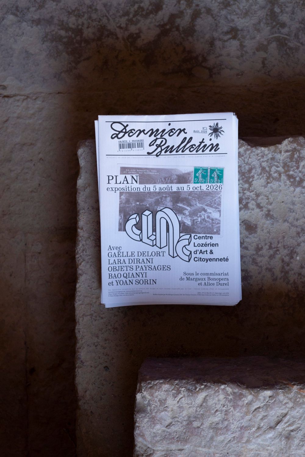 Dernier Bulletin n° 1, août 2026, « PLAN, exposition du 5 août au 5 oct. 2026 », CLAC, posé sur des pierres