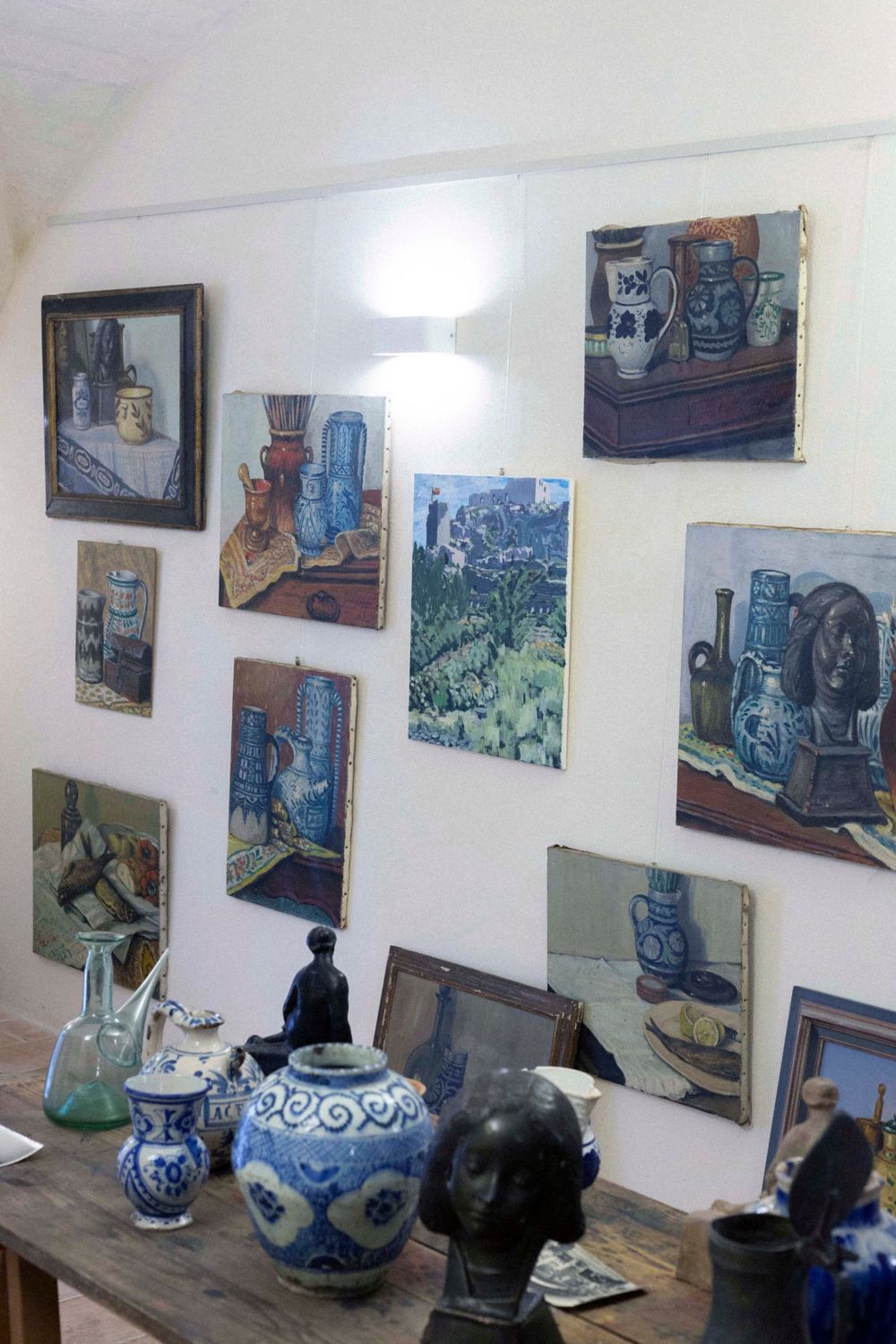 Intérieur–Extérieur : mur de natures mortes de Louis Jou et vue peinte des Baux-de-Provence, au-dessus de la table d’objets