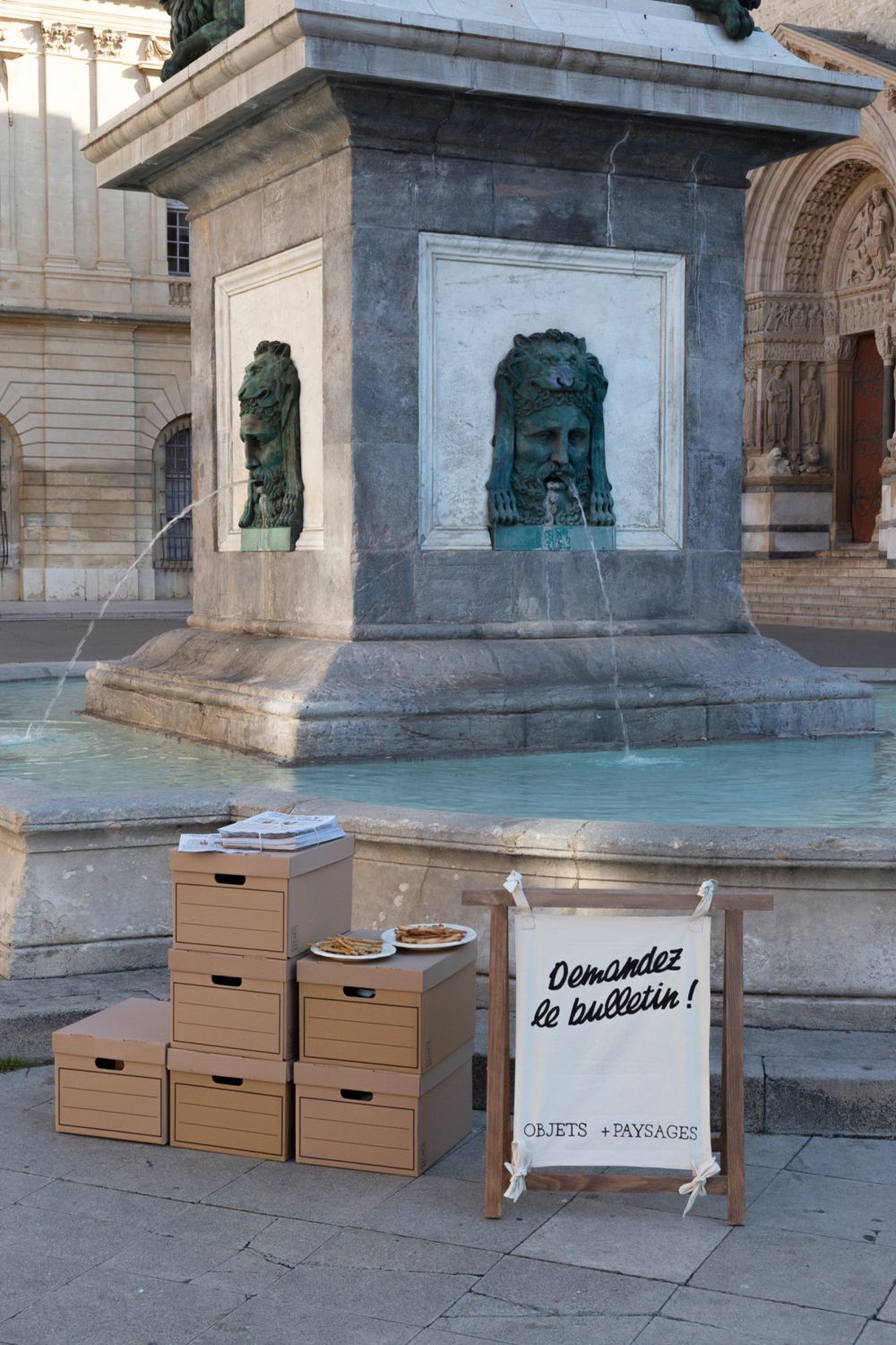 Premier Bulletin présenté sur des boîtes d’archives devant la fontaine de la place de la République, Arles